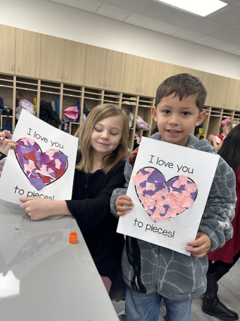 two students smiling and holding a valentine's art project