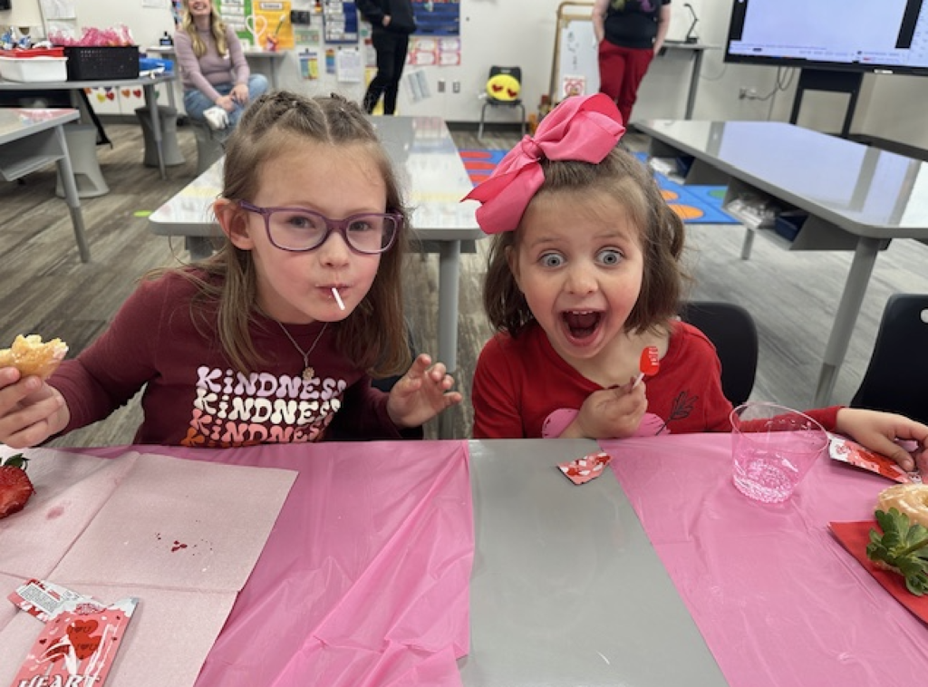 two students smiling and eating a valentine's snack