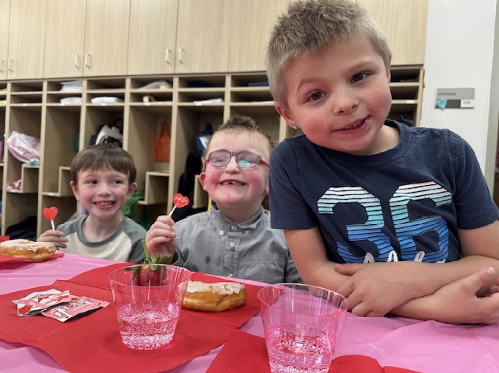 three students smiling and eating a valentine's snack