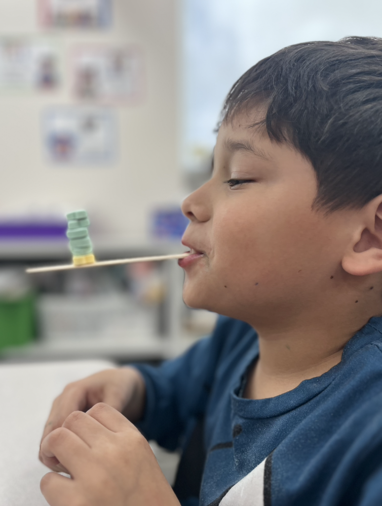 student holding and balancing candy hearts on a popsicle stick 