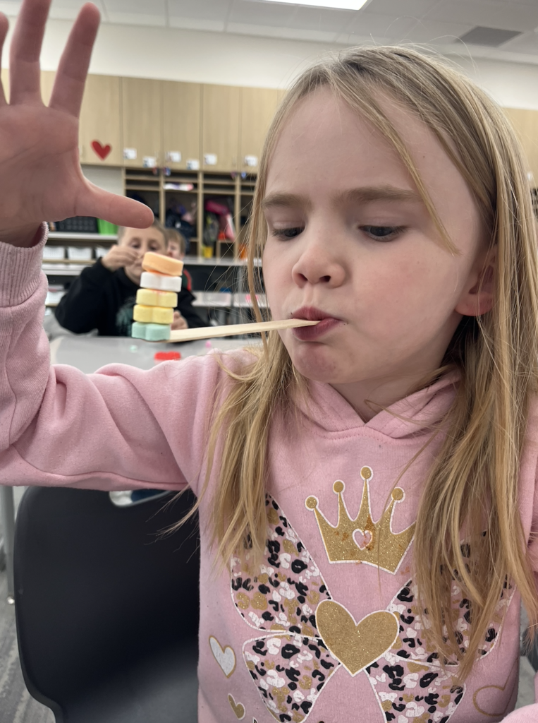 student holding and balancing candy hearts on a popsicle stick 
