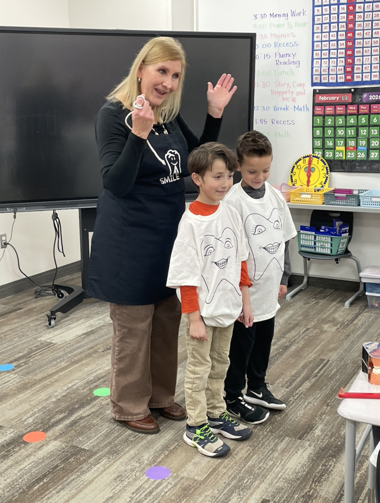 two students standing with the school nurse. They are wearing tooth shirts and are pretending to be teeth that are flossed
