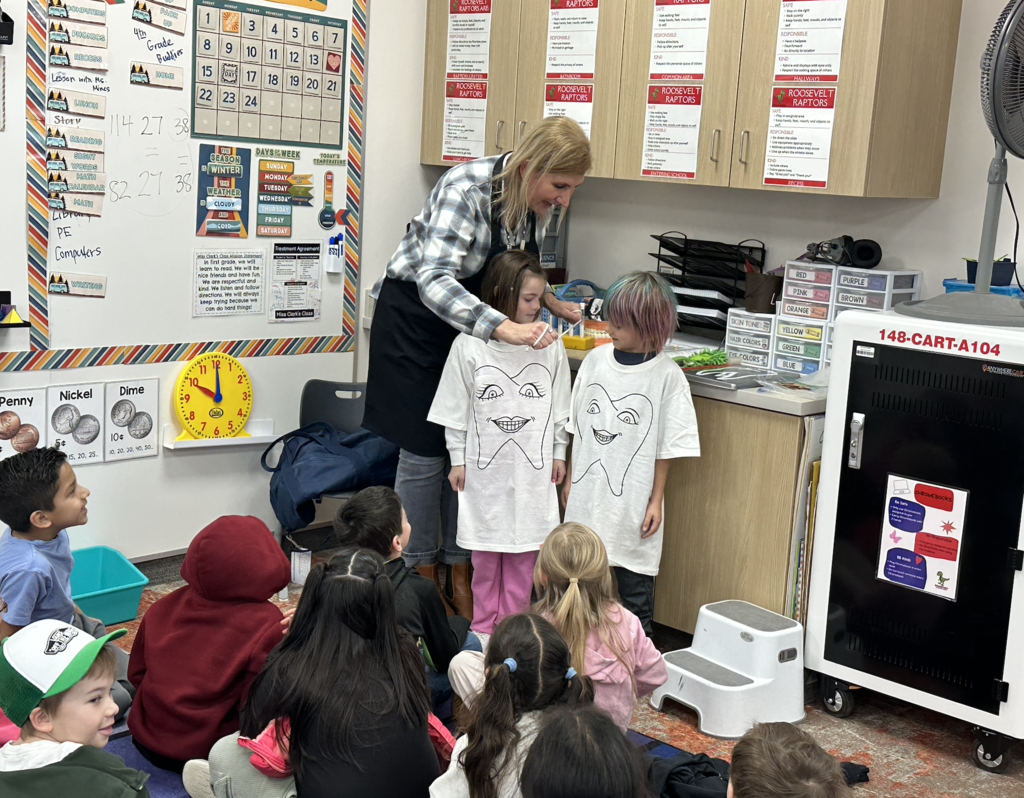 two students standing with the school nurse. They are wearing tooth shirts and are pretending to be teeth that are flossed