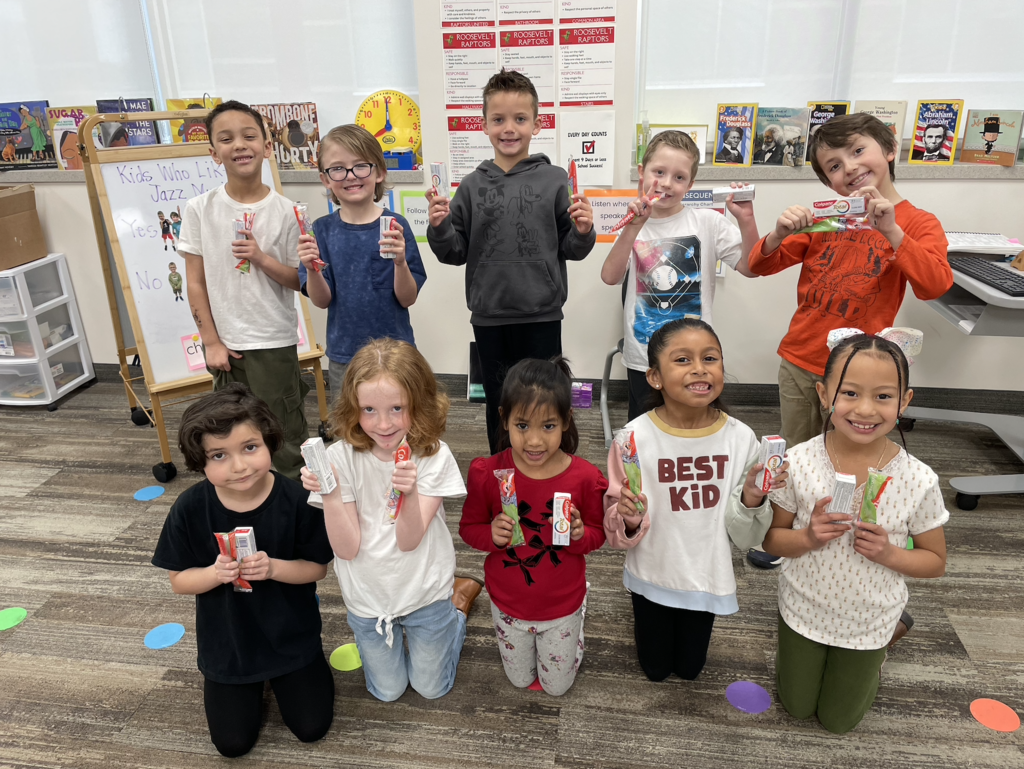 first grade class standing all together holding their new toothbrushes and toothpaste 