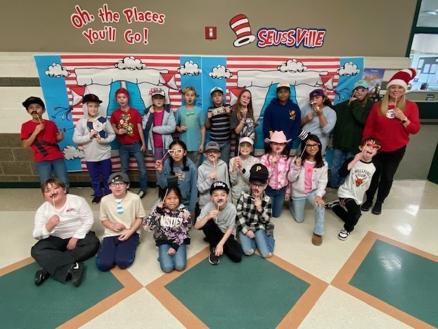 Mrs. Anderson's class in front of a Dr. Seuss banner holding different props.