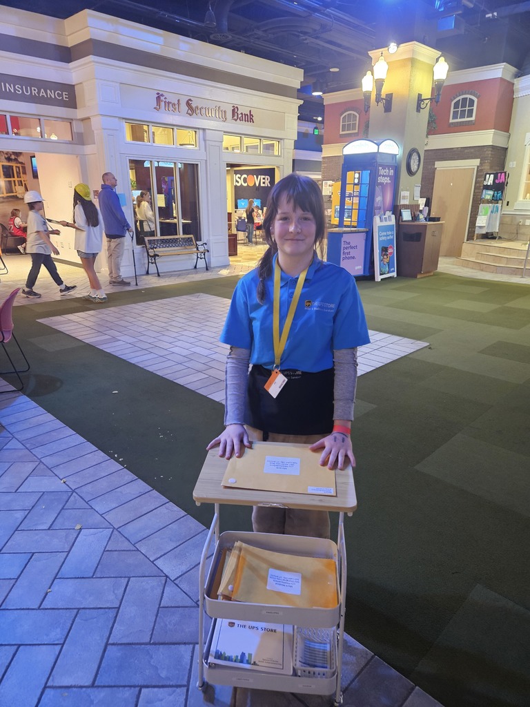 A student employee of "The UPS Store" at BizTown stands proudly with a delivery cart full of yellow envelopes in a simulated city square.