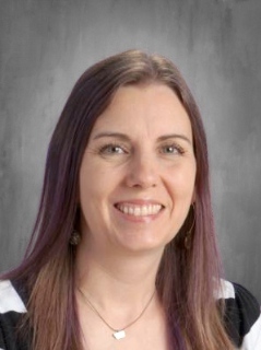A headshot of Lomond View Elementary librarian, Mrs. McKinney, smiling warmly. She has long hair with purple highlights and is wearing a black and white striped top.