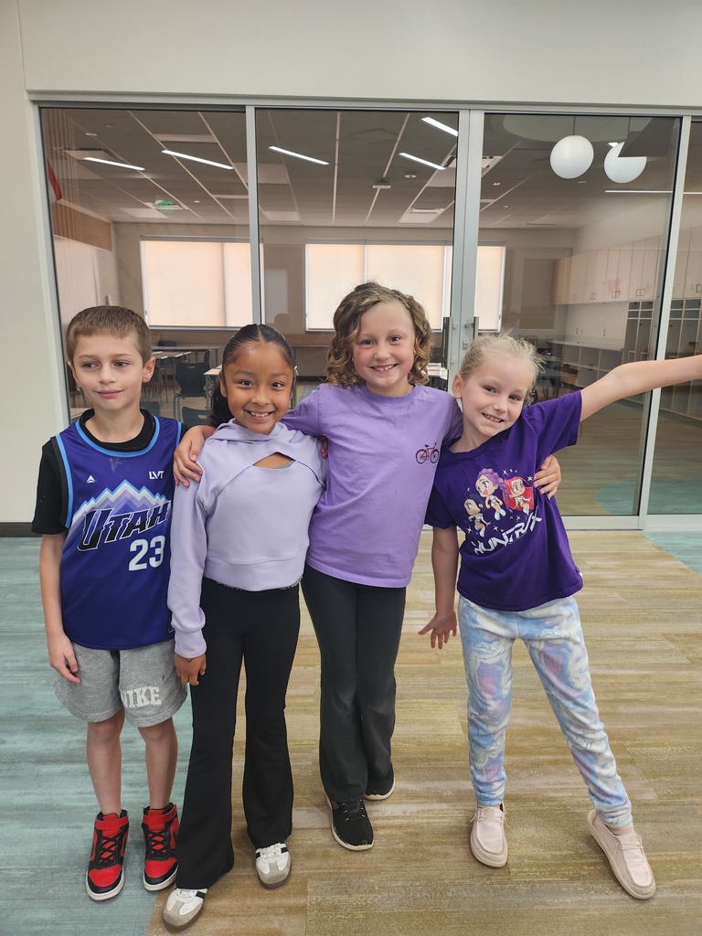 Four elementary students (one boy and three girls) pose together with their arms around each other.