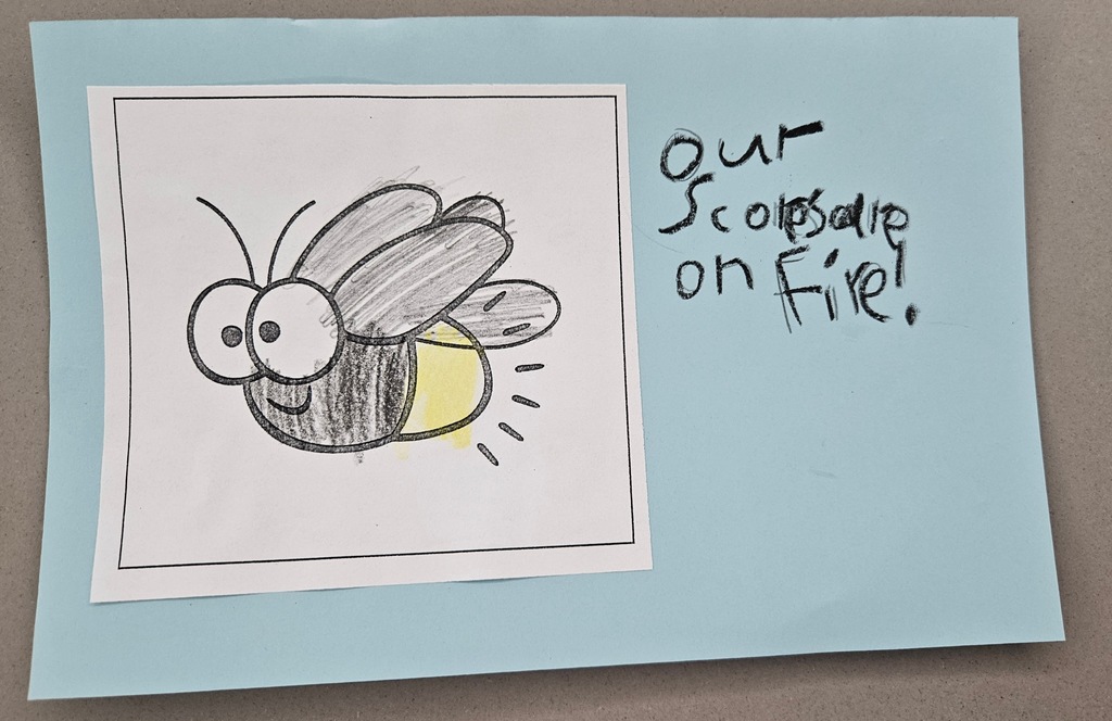 A hand-colored drawing of a firefly with a glowing yellow tail. Handwritten text on a blue background reads: "Our Scores are on Fire!"
