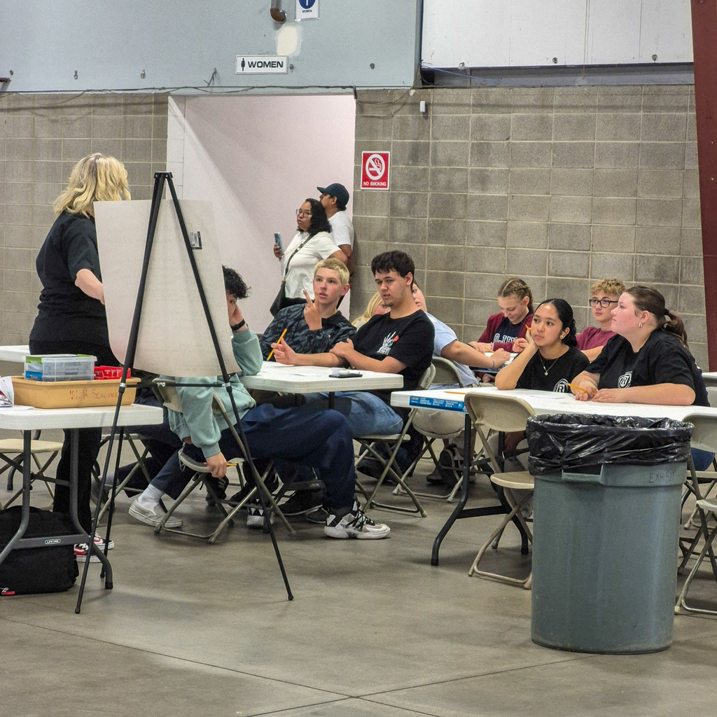 A classroom-style setup where students are seated at tables, listening intently to a presentation or instructions during the district competition.