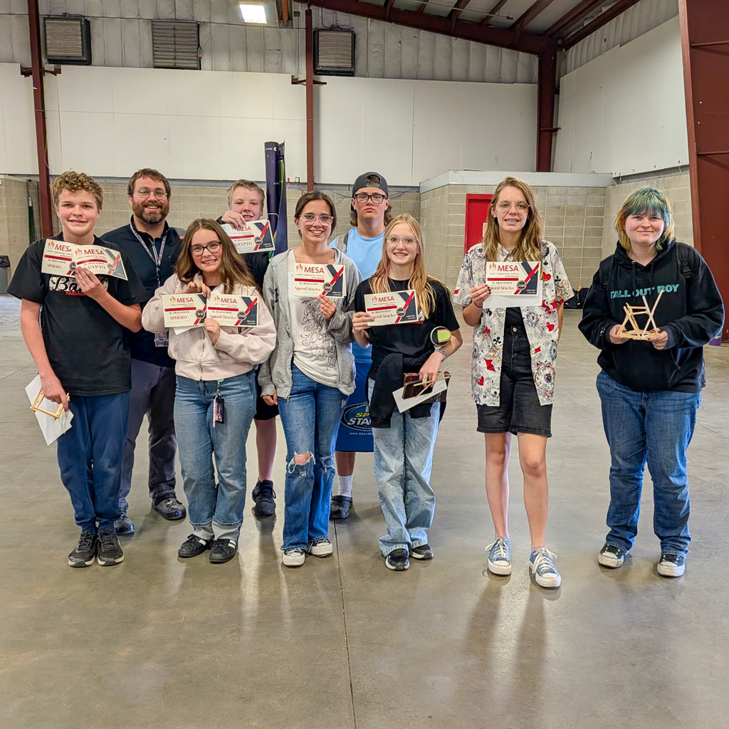 A group of winning students and their advisor stand together indoors, smiling and holding up their official MESA certification and prize envelopes.