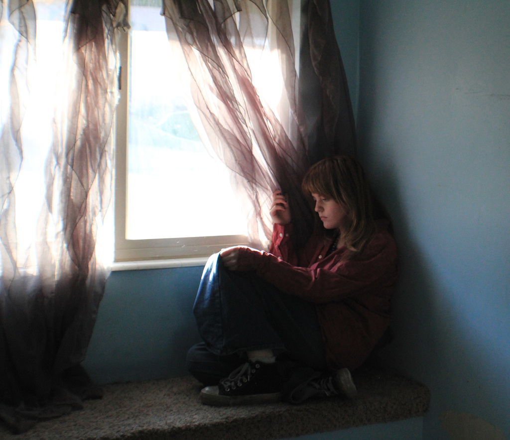 Student sitting by window holding the curtain back