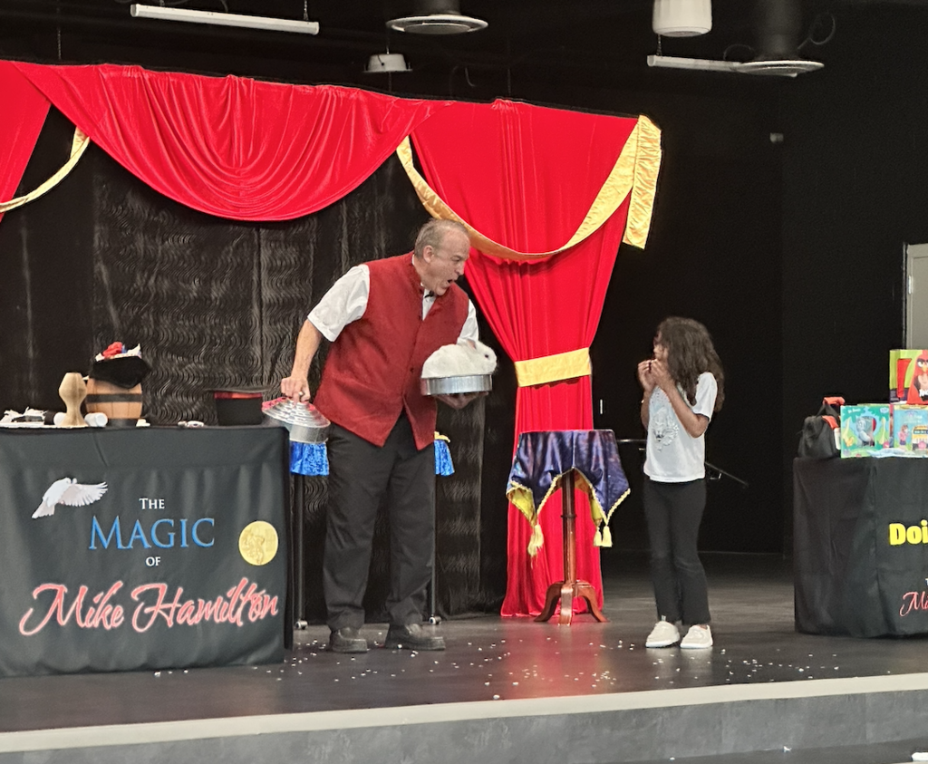 student on stage with the magician with a surprised look on her face as a bunny magically appears 