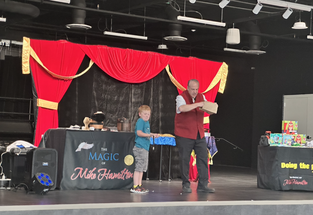 student on stage with a magician showing a confused look on his face