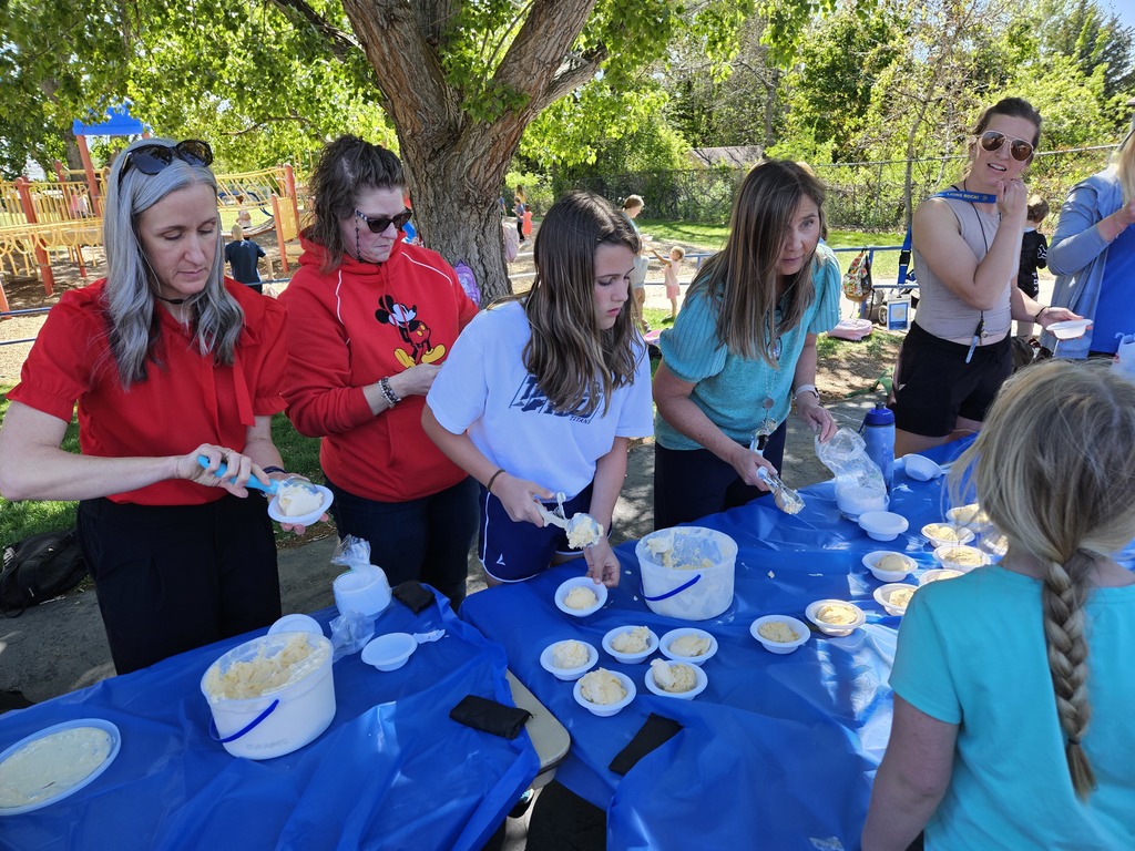Volunteers at a table covered in a blue cloth scoop bowls of vanilla ice cream for the students after the race.