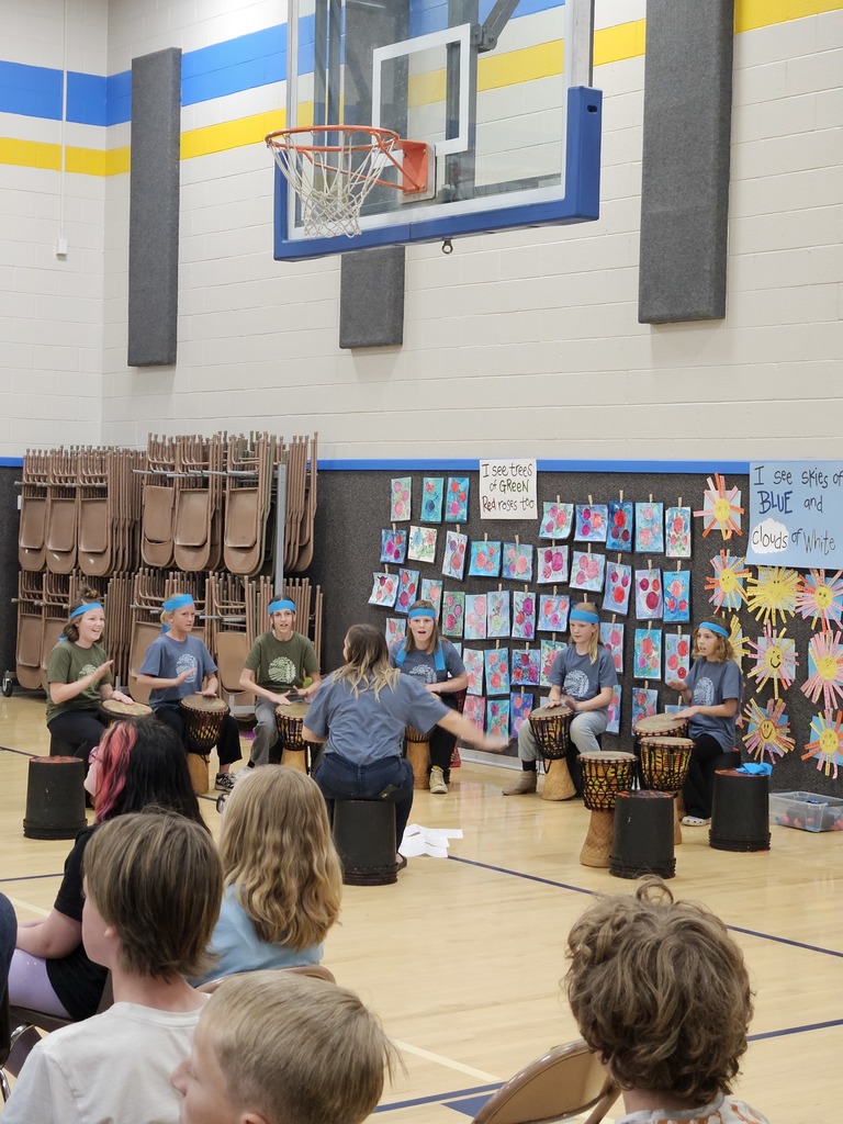 A specialized group of students wearing blue headbands sit in a circle on the gym floor playing Djembe drums.
