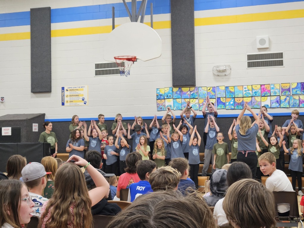 A group of students in blue shirts clapping their hands high above their heads in unison during a song.