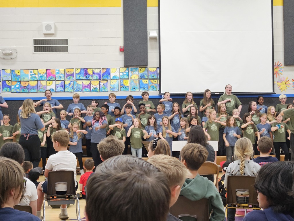The full choir on stage performing choreographed hand motions during the assembly.
