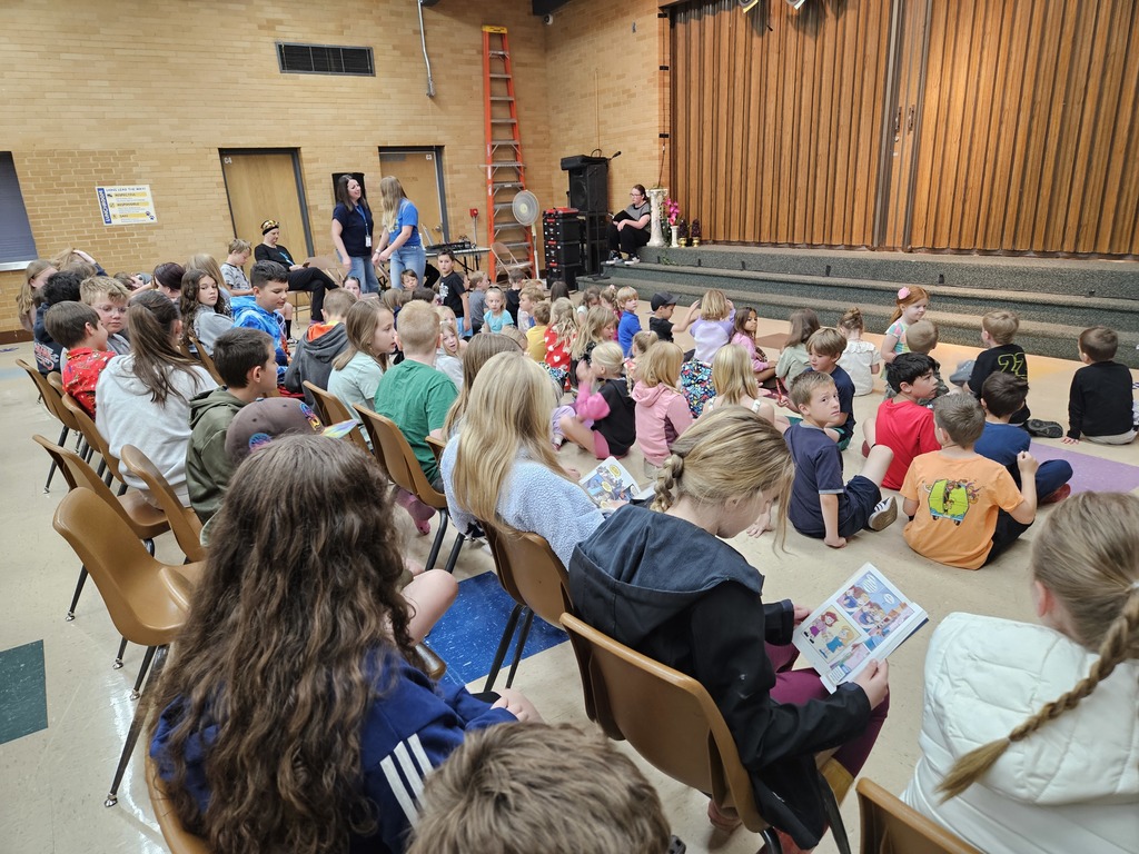 A view of a large audience of young children sitting on the floor and in chairs, focused intently on the stage before the start of the performance.