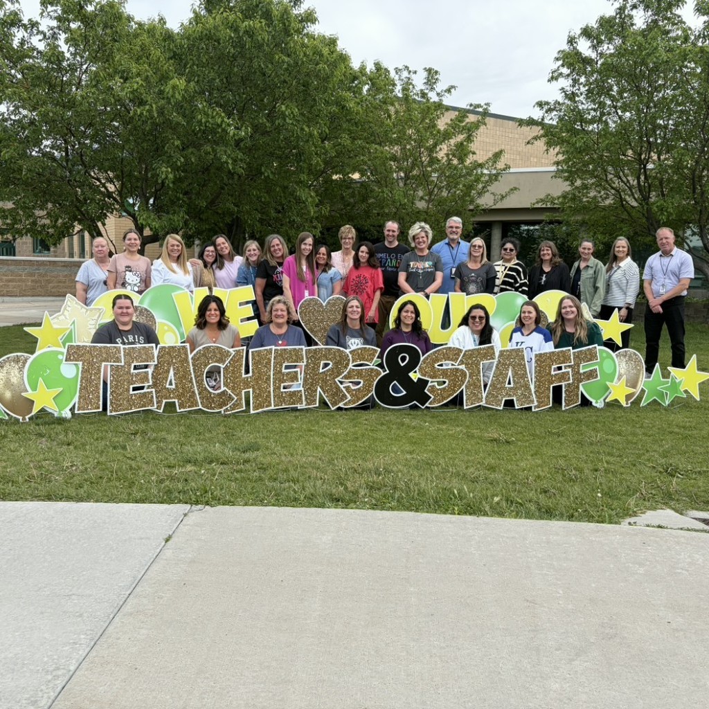 teacher standing by a sign that says We love our teachers and staff