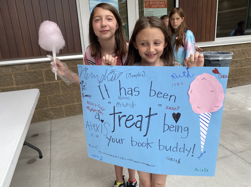 two girls holding a sign saying "it has been a treat being your book buddy!" and holding the cotton candy that they made