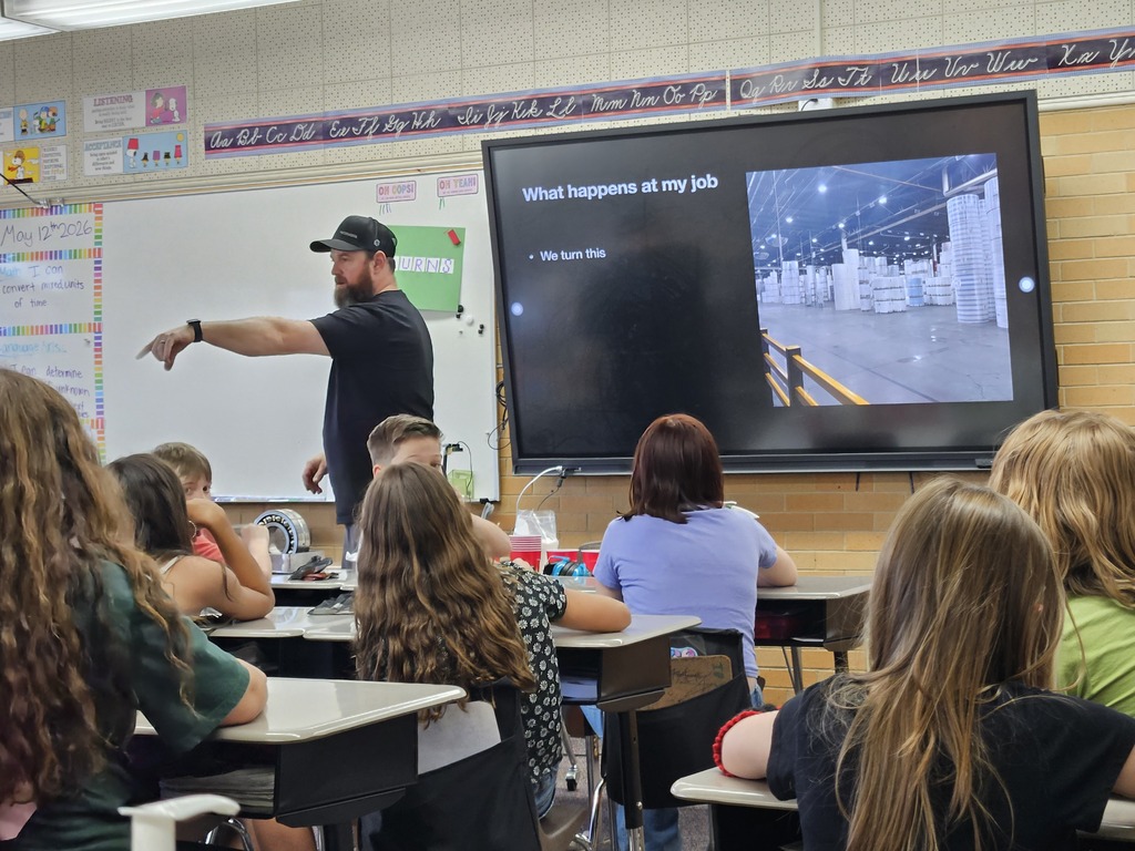  A presenter in a baseball cap shows a slide of a large industrial warehouse with rolls of materials.