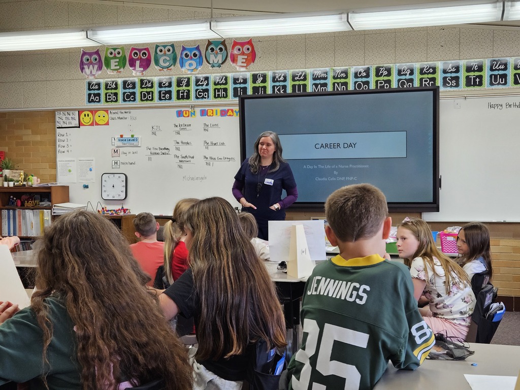  A nurse practitioner in navy scrubs stands in front of a screen that reads "Career Day: A Day in the Life of a Nurse Practitioner."