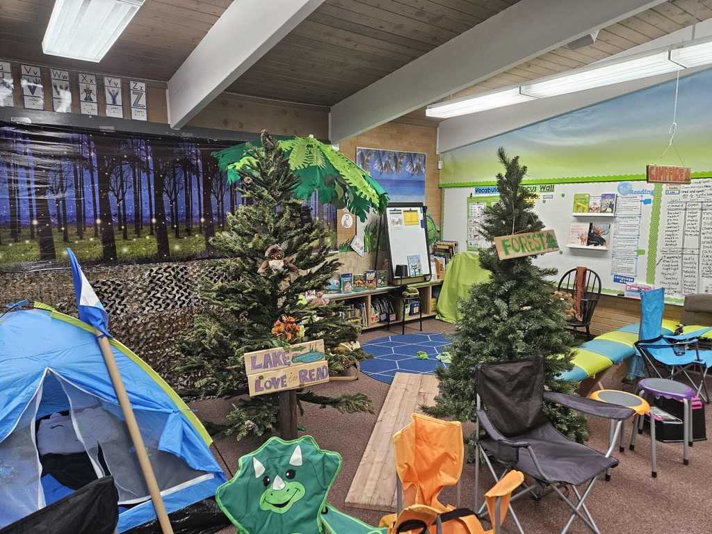 A decorated corner of the classroom featuring evergreen trees, a "Lake Love to Read" sign, and a blue tent. A forest backdrop creates an immersive outdoor feel.