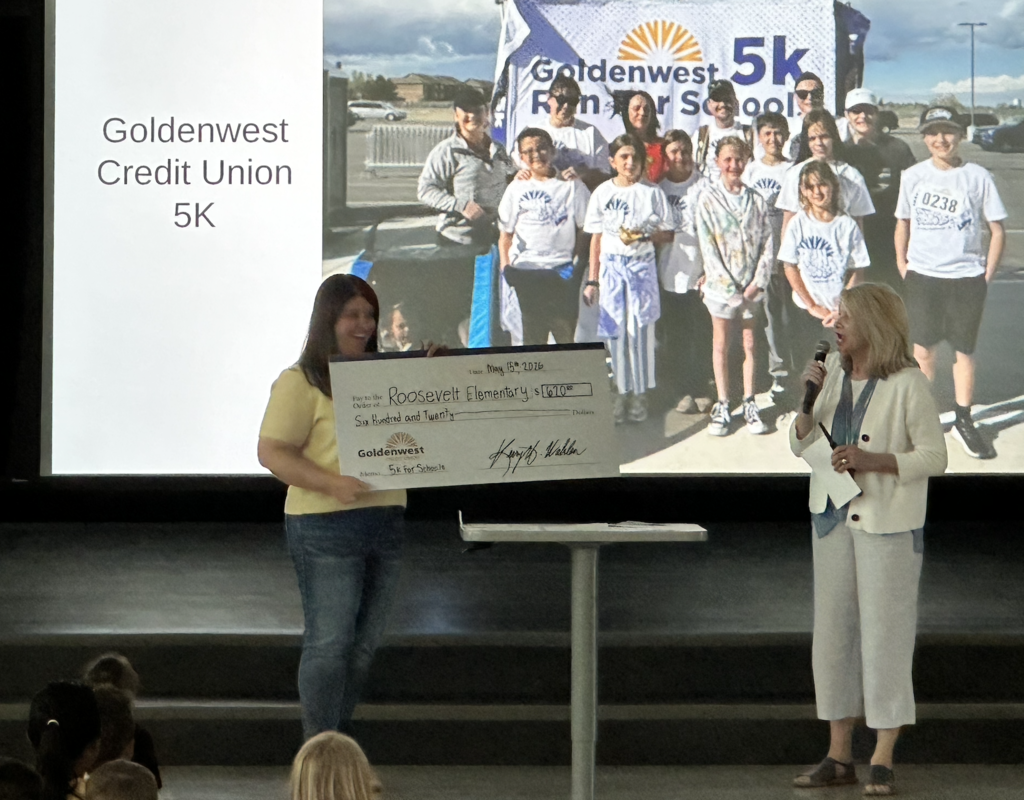the bank representative and the school principal standing in front of the school with a big check