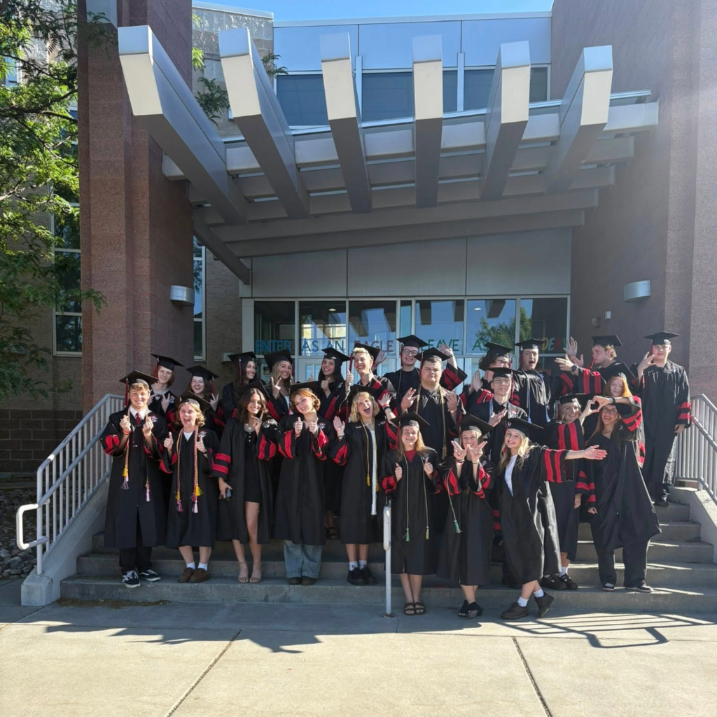 Picture of seniors in the cap and gown on the front stairs of the school.