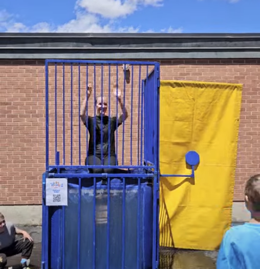 A series of photos showing Dr. Watson, the principal of Lomond View Elementary, participating in a dunk tank event on a sunny day. She is wearing a black shirt and sitting on the collapsible platform above a large blue water tank. One photo captures the moment a student hits the target, and subsequent photos show Dr. Watson submerged in the water and then emerging with a big smile while students cheer her on.