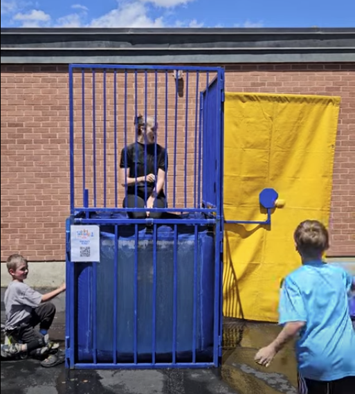 A series of photos showing Dr. Watson, the principal of Lomond View Elementary, participating in a dunk tank event on a sunny day. She is wearing a black shirt and sitting on the collapsible platform above a large blue water tank. One photo captures the moment a student hits the target, and subsequent photos show Dr. Watson submerged in the water and then emerging with a big smile while students cheer her on.