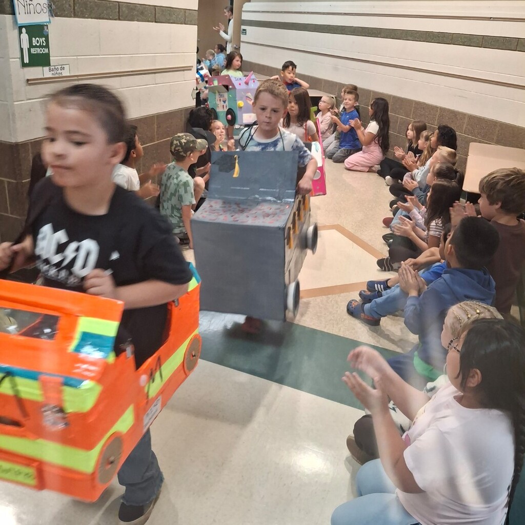 Kids watching kindergartners in their cardboard cars 