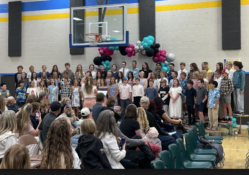 All of 6th grade on risers performing a song and being led by the music teacher.