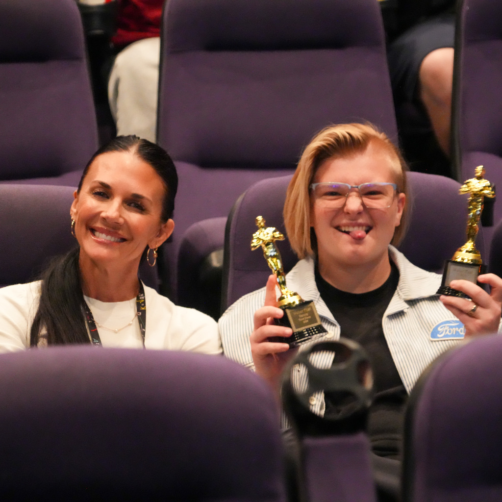 A student holding two awards sitting next to the principal