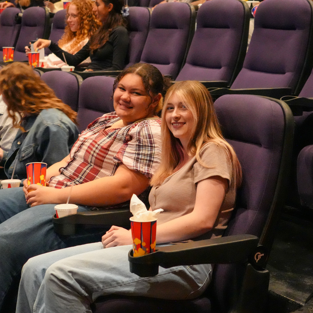 A group of students sitting in the theater smiling towards the camera