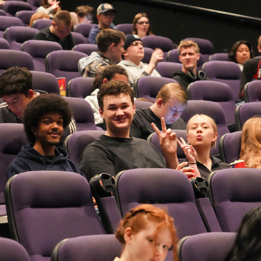 A group of students sitting in the theater smiling towards the camera