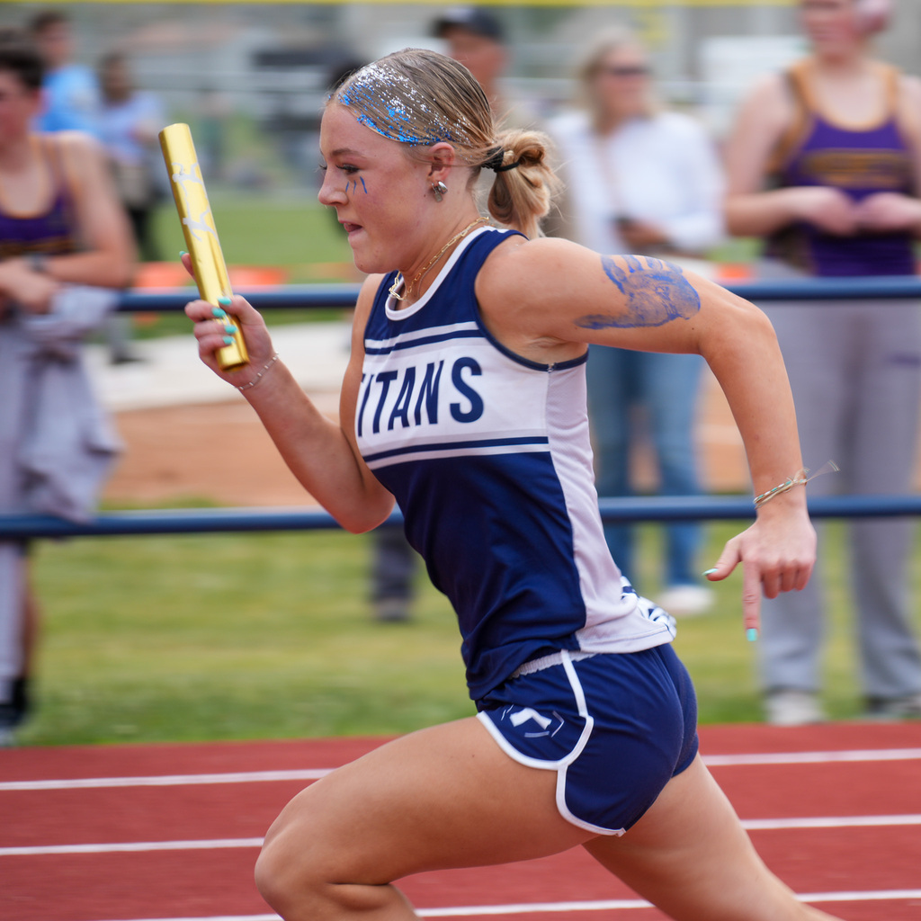 An orion girl's track athlete runs by holding the baton with a blurred background