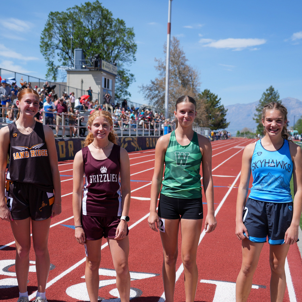 Four girl athletes stand at the starting line with smiles