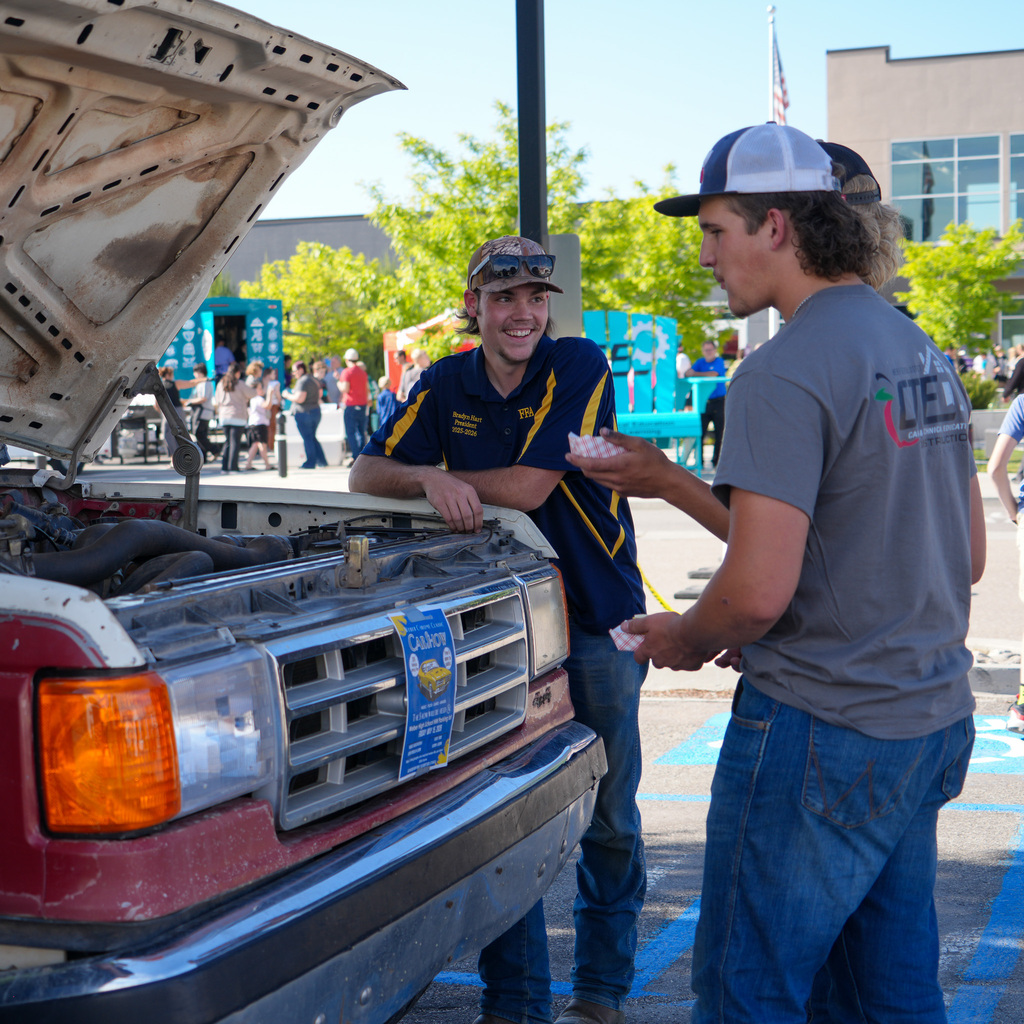 Three students stand around an open vehicle hood