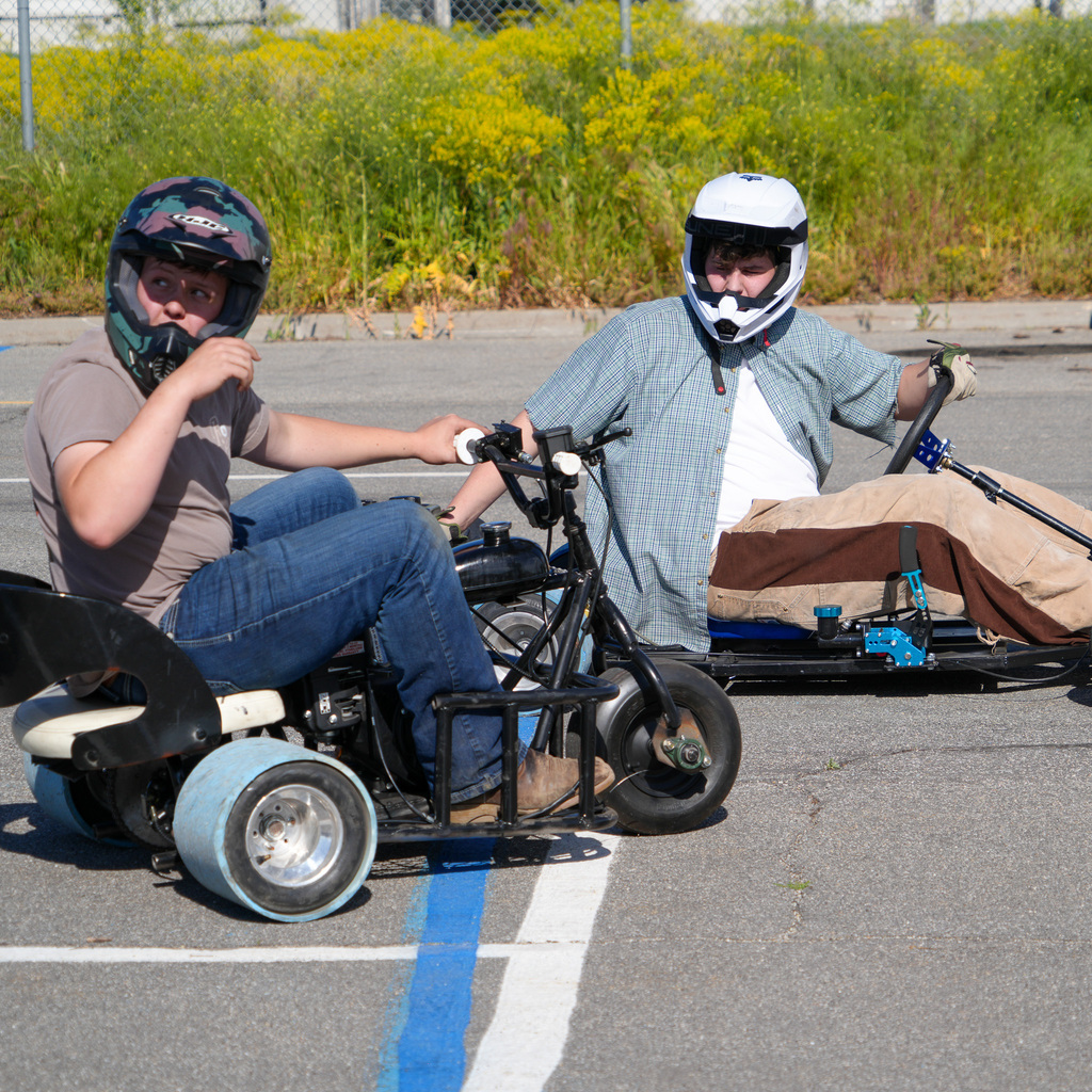 Two kids on drift trikes wearing helmets look up for instruction