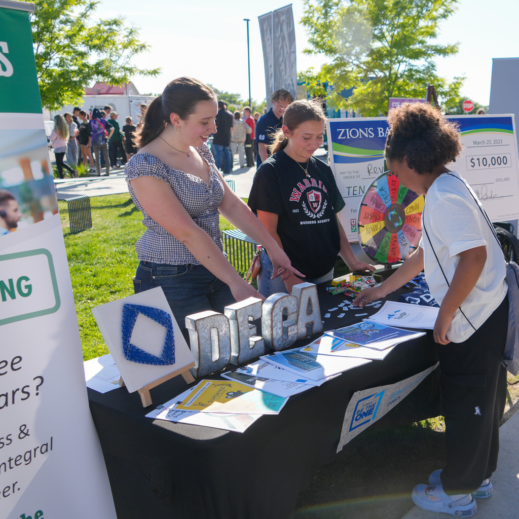 Two students at the DECA booth talk to another student