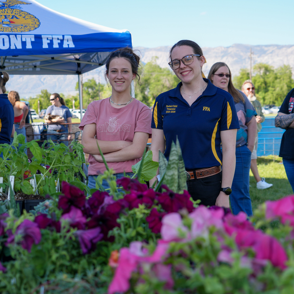 Two students smile behind a row of flowers
