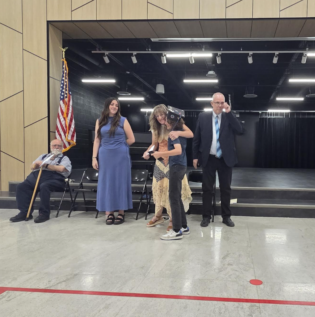 6th grade teacher giving a side hug to a graduating 6th grade student