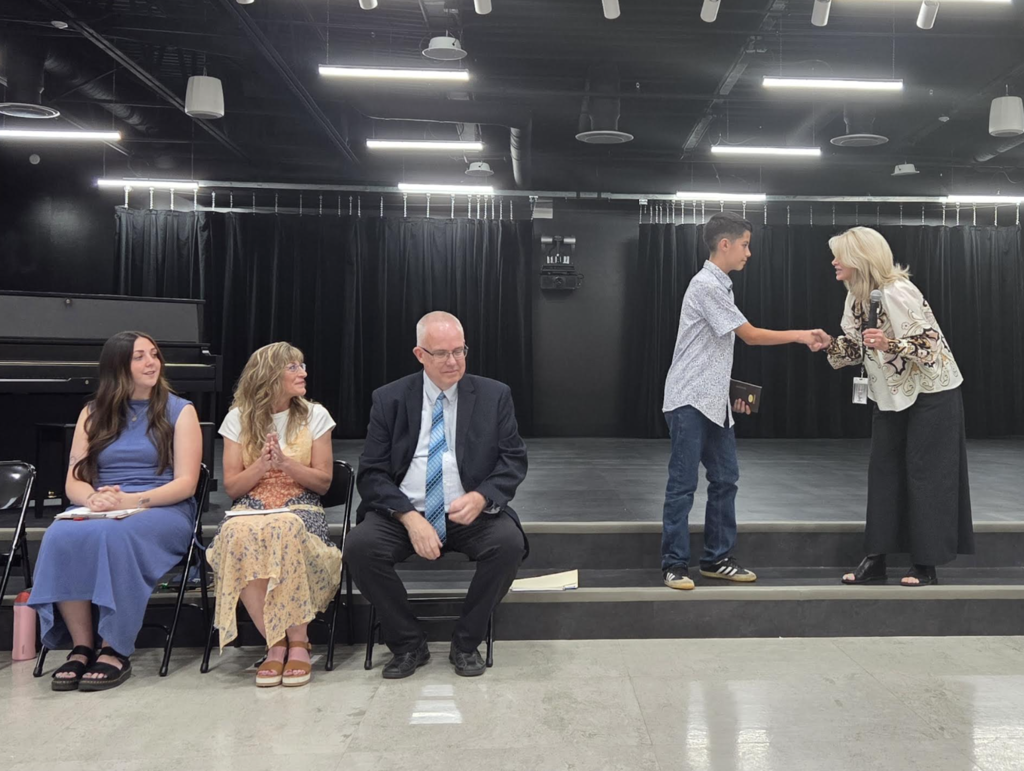 school principal shaking hands with a graduating 6th grade student while 6th grade teachers watch