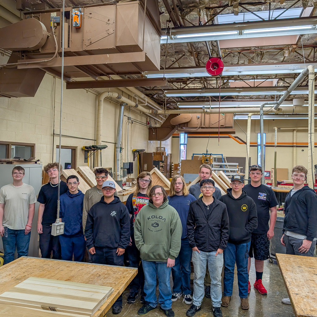 A group of students stand in wood shop with the tiny libraries behind them