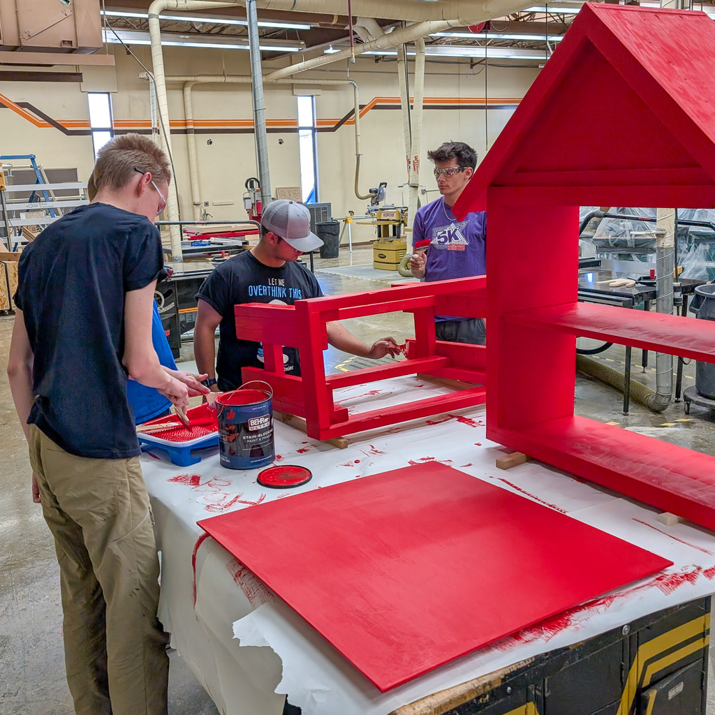 Students are painting a tiny library in a wood shop