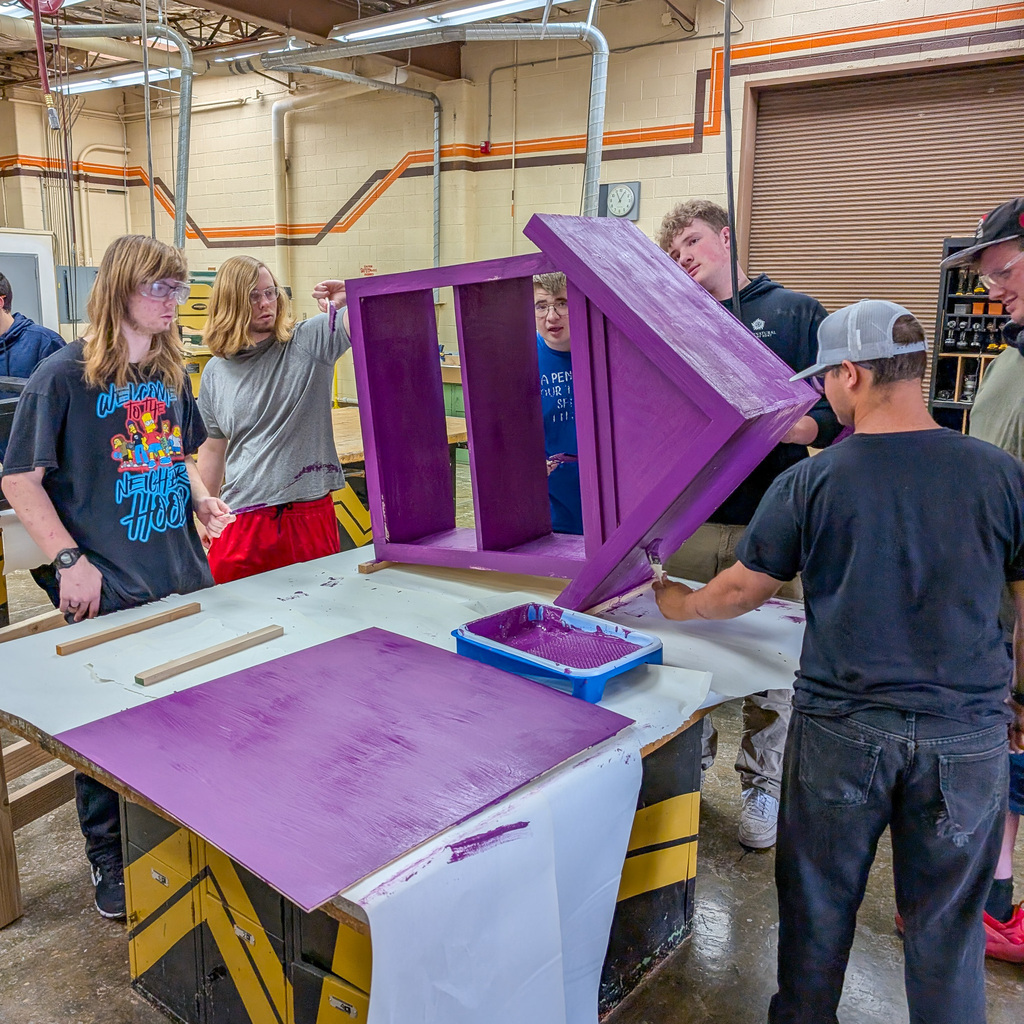 Students are painting a tiny library in a wood shop