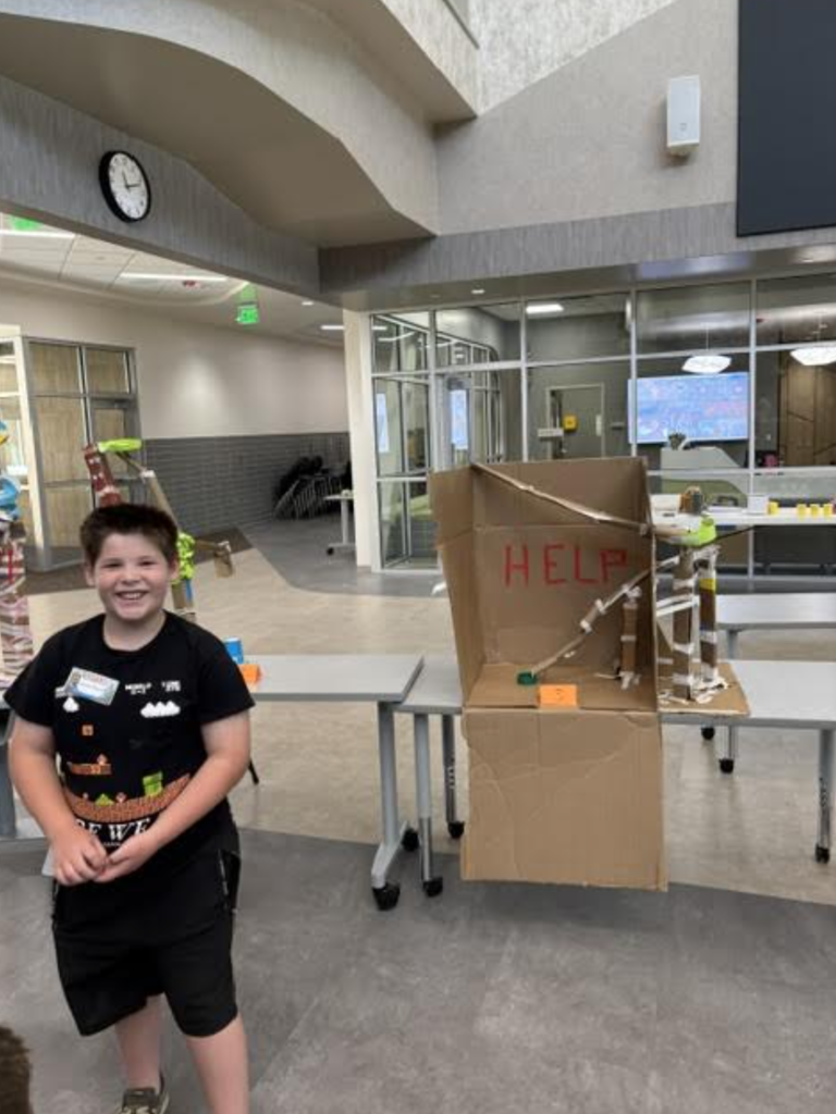 student standing with the roller coaster that they built for STEAM Camp