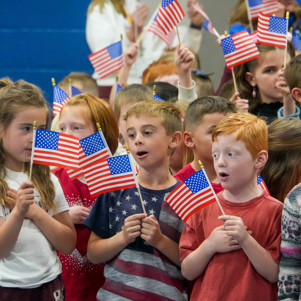 A group of students holding small American flags singing